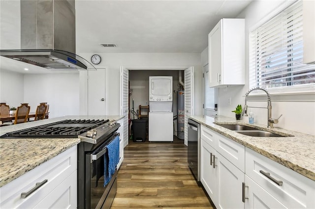 kitchen with stainless steel appliances, dark wood-type flooring, a sink, stacked washer / drying machine, and wall chimney range hood