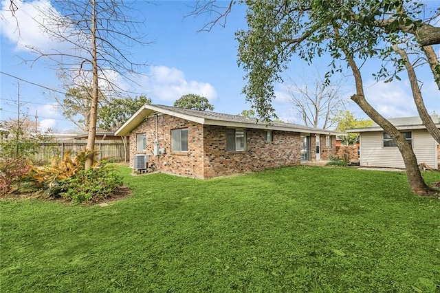 back of property with brick siding, a lawn, central AC, and fence