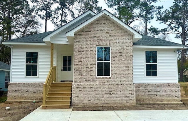 view of front of property featuring brick siding and roof with shingles