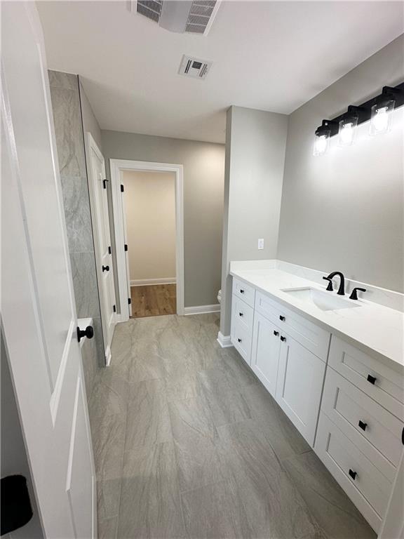 bathroom featuring toilet, vanity, visible vents, and baseboards