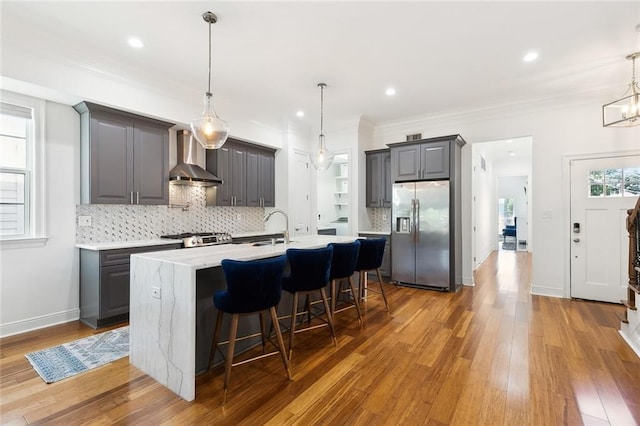 kitchen featuring gray cabinets, stove, wall chimney range hood, stainless steel fridge, and a wealth of natural light