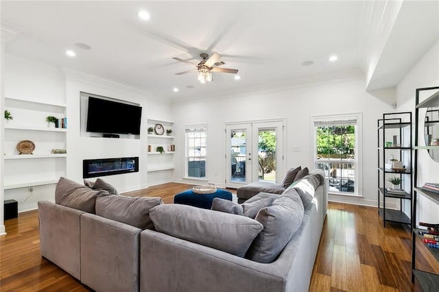 living room with a glass covered fireplace, built in shelves, dark wood finished floors, and a healthy amount of sunlight