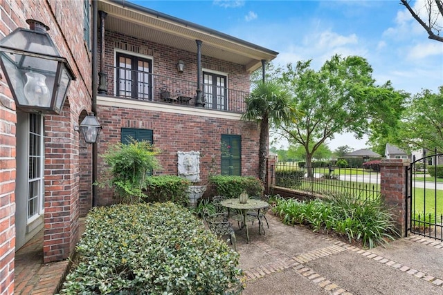 view of side of home with a balcony, a gate, fence, and brick siding