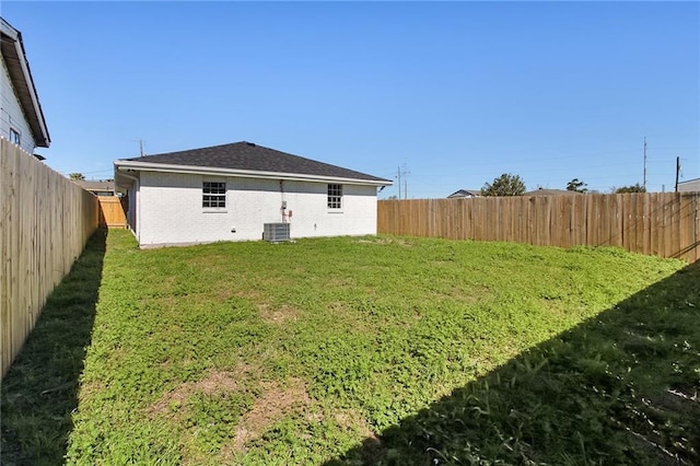 rear view of house featuring a yard, brick siding, cooling unit, and a fenced backyard