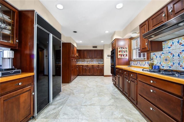 kitchen featuring visible vents, black appliances, glass insert cabinets, under cabinet range hood, and tasteful backsplash