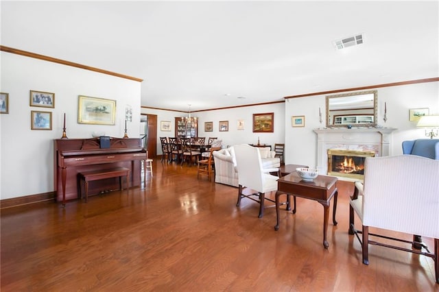 living area with visible vents, wood finished floors, a glass covered fireplace, crown molding, and baseboards