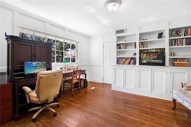 office area with a decorative wall, built in shelves, wood finished floors, and visible vents