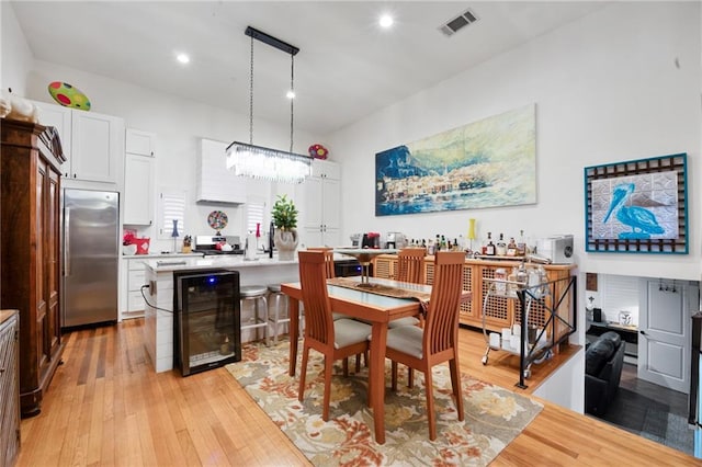 dining space featuring visible vents, beverage cooler, light wood-type flooring, and a chandelier