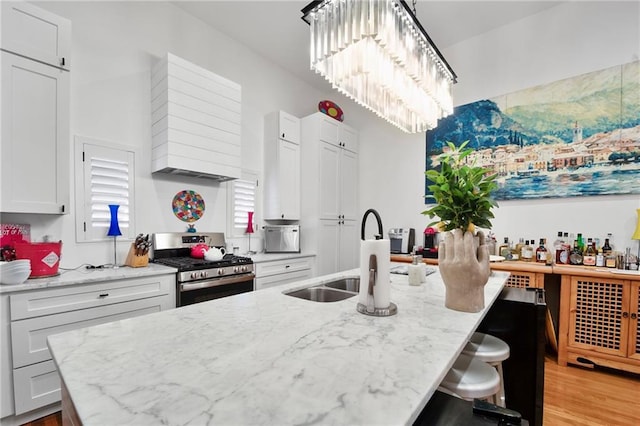 kitchen with a kitchen island with sink, gas range, light stone counters, custom exhaust hood, and a sink