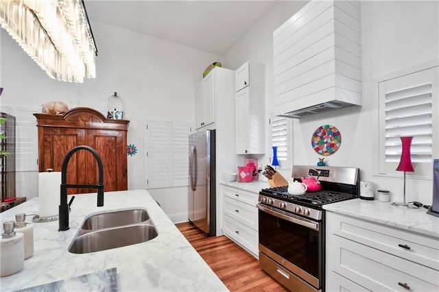 kitchen featuring light stone counters, stainless steel appliances, light wood-style floors, white cabinetry, and a sink