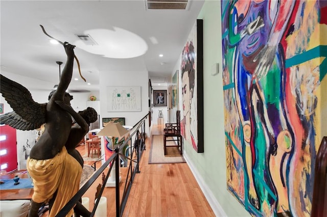 hall featuring light wood-type flooring, visible vents, an upstairs landing, and baseboards