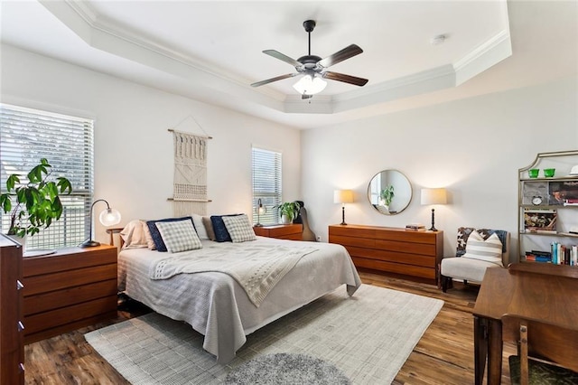 bedroom with a ceiling fan, a tray ceiling, wood finished floors, and ornamental molding