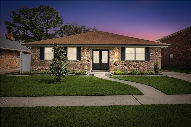 ranch-style house featuring french doors, brick siding, a lawn, and a shingled roof