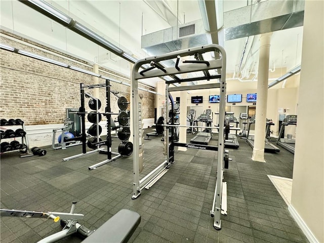 workout area featuring brick wall, visible vents, and a towering ceiling