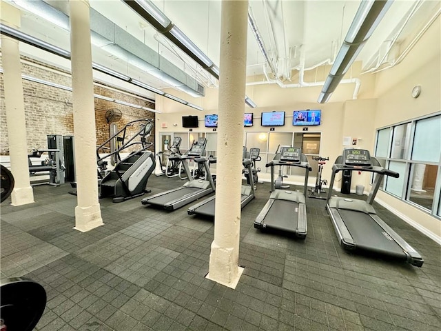 exercise room featuring brick wall, decorative columns, and a towering ceiling