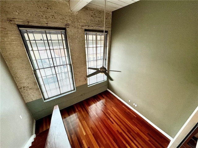 empty room featuring beamed ceiling, baseboards, ceiling fan, and wood finished floors