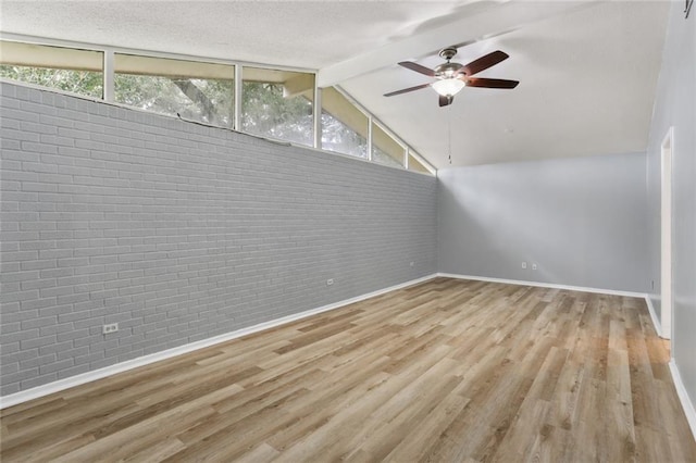 spare room featuring lofted ceiling with beams, wood finished floors, a healthy amount of sunlight, and brick wall