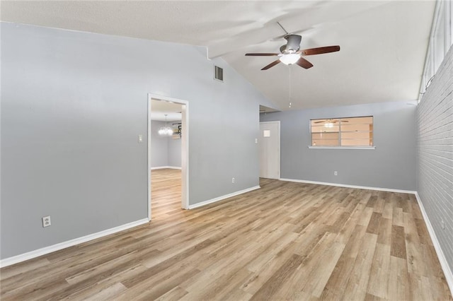 spare room featuring light wood-type flooring, visible vents, lofted ceiling, and ceiling fan with notable chandelier