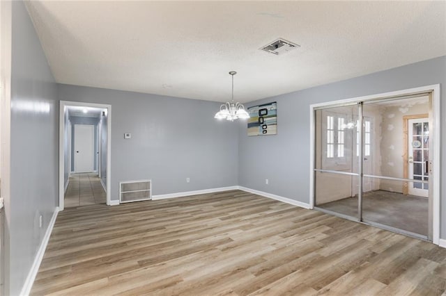 unfurnished dining area with visible vents, a textured ceiling, light wood-type flooring, and an inviting chandelier