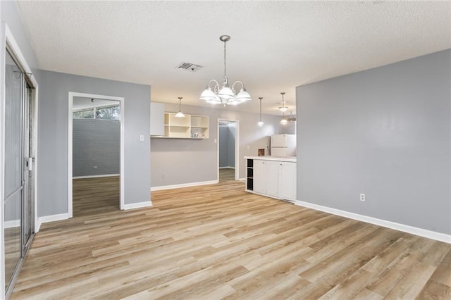 unfurnished living room featuring visible vents, baseboards, an inviting chandelier, a textured ceiling, and light wood-type flooring