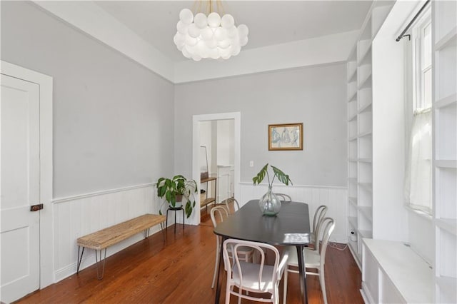 dining area with an inviting chandelier, wood finished floors, and wainscoting