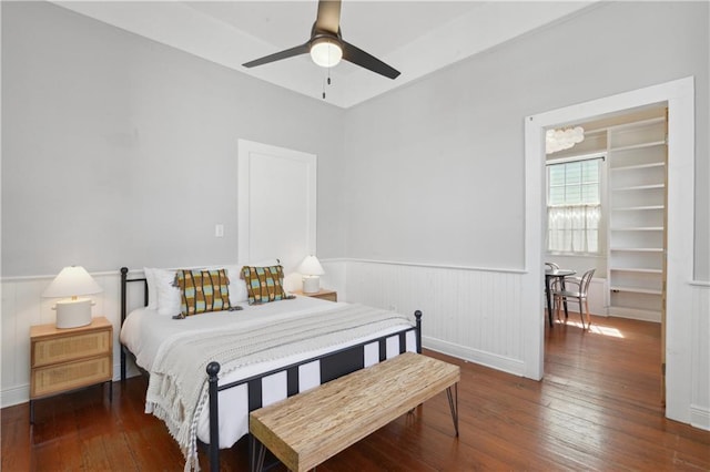 bedroom featuring a wainscoted wall, hardwood / wood-style floors, and a ceiling fan