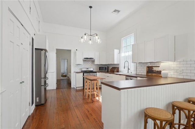 kitchen featuring dark wood-style floors, visible vents, a peninsula, stainless steel appliances, and under cabinet range hood