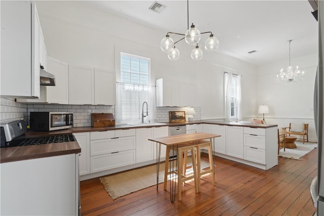 kitchen with visible vents, a peninsula, a sink, stainless steel appliances, and butcher block countertops