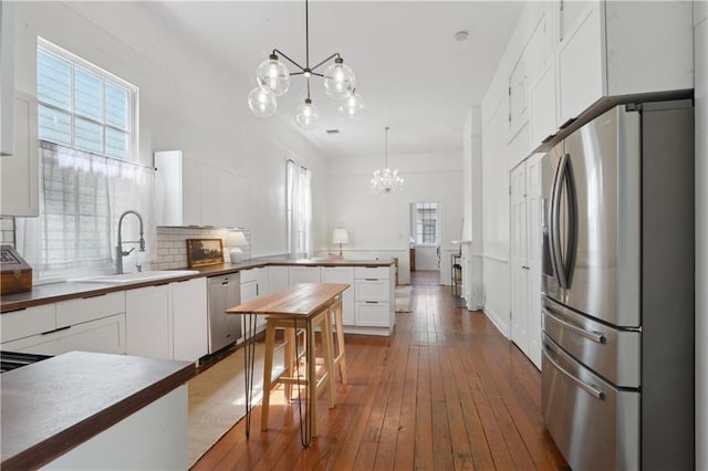 kitchen featuring a peninsula, stainless steel appliances, an inviting chandelier, white cabinetry, and a sink