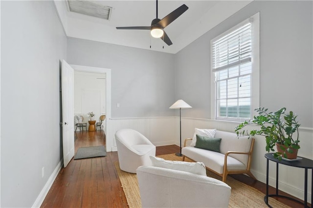 sitting room featuring ceiling fan, visible vents, a wainscoted wall, and hardwood / wood-style flooring