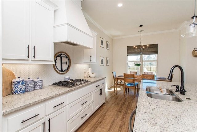 kitchen featuring stainless steel gas cooktop, custom exhaust hood, light wood-style flooring, a sink, and crown molding