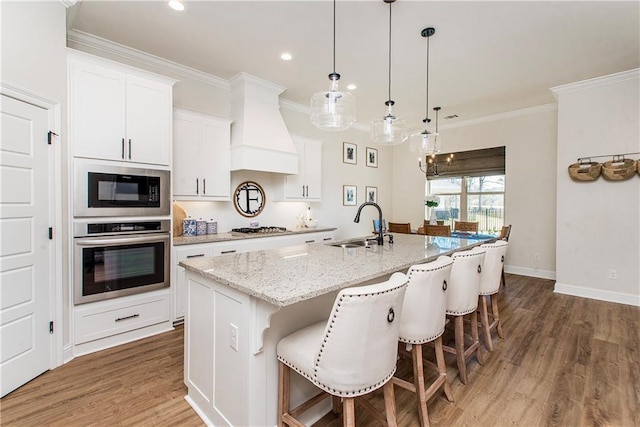 kitchen featuring crown molding, an island with sink, custom range hood, stainless steel appliances, and a sink