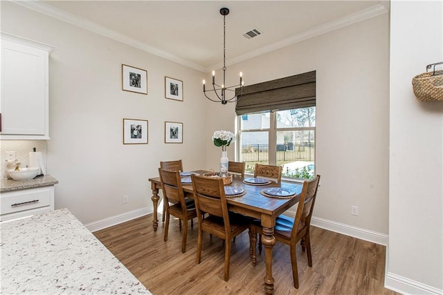 dining area featuring visible vents, a notable chandelier, ornamental molding, wood finished floors, and baseboards