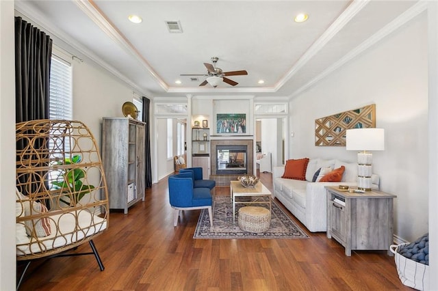 living area with wood finished floors, visible vents, ornamental molding, a tiled fireplace, and a raised ceiling