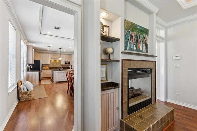 kitchen featuring light wood-type flooring, baseboards, ornamental molding, and a tiled fireplace