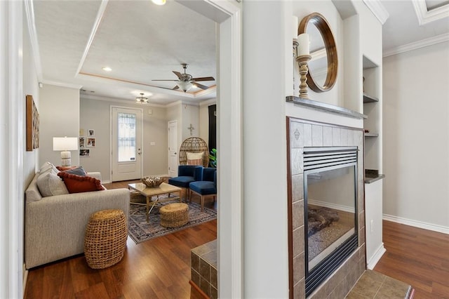 living room with a tray ceiling, ornamental molding, wood finished floors, and a tile fireplace