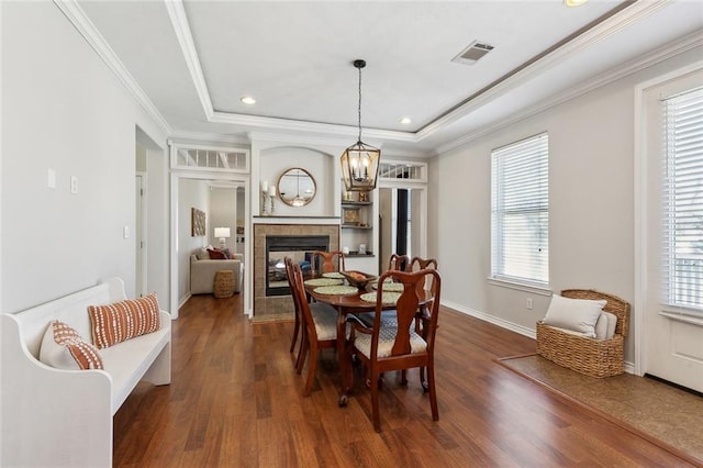 dining area featuring dark wood finished floors, a raised ceiling, visible vents, and a tiled fireplace