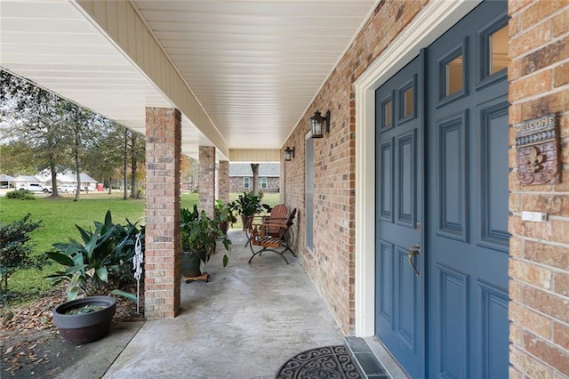 entrance to property featuring a porch, a yard, and brick siding