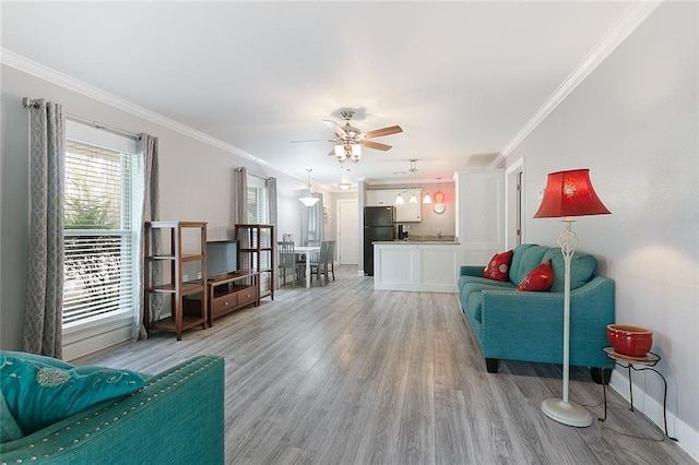 living area with crown molding, light wood-style flooring, a ceiling fan, and baseboards