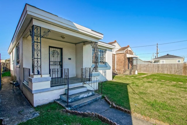 view of front of house featuring stucco siding, covered porch, a front yard, and fence