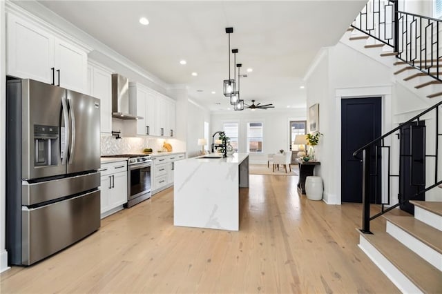 kitchen with white cabinetry, wall chimney exhaust hood, appliances with stainless steel finishes, and a sink