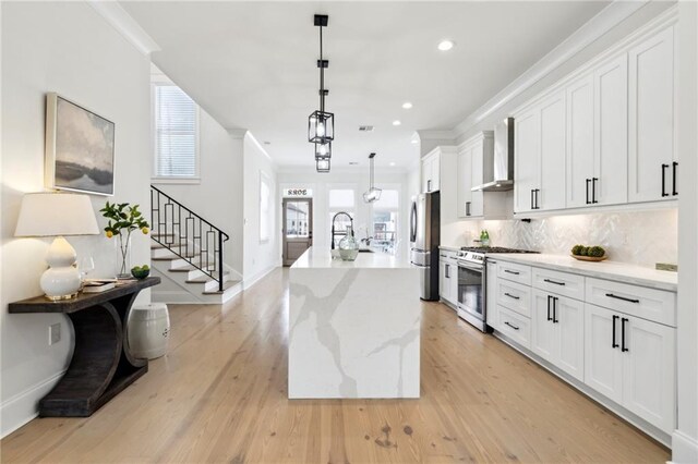 kitchen with tasteful backsplash, ornamental molding, light wood-style floors, stainless steel appliances, and wall chimney exhaust hood