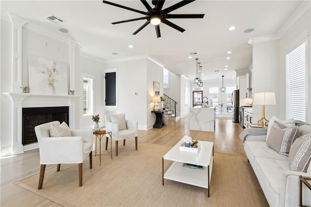 living area featuring visible vents, a fireplace, light wood-type flooring, and crown molding