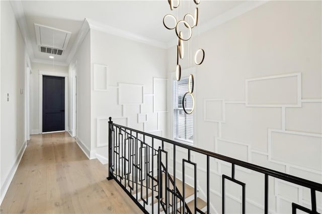 hallway featuring visible vents, attic access, light wood-type flooring, ornamental molding, and an upstairs landing