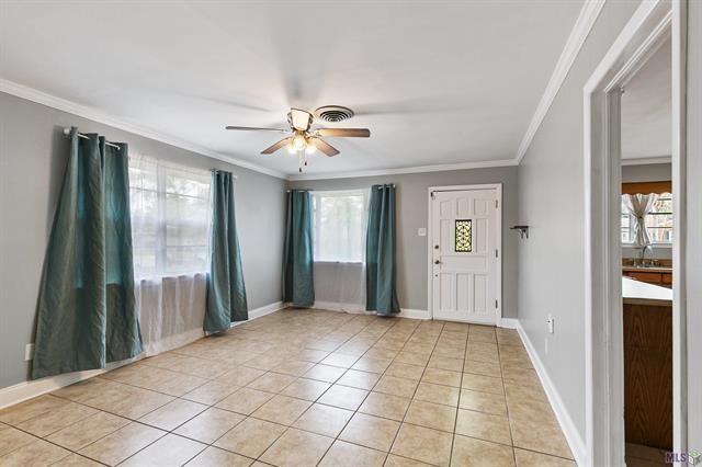 empty room featuring visible vents, baseboards, a ceiling fan, crown molding, and light tile patterned floors