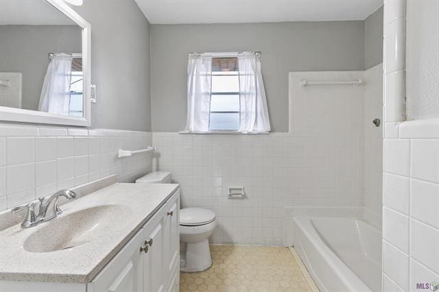 full bath with toilet, a healthy amount of sunlight, vanity, and tile walls