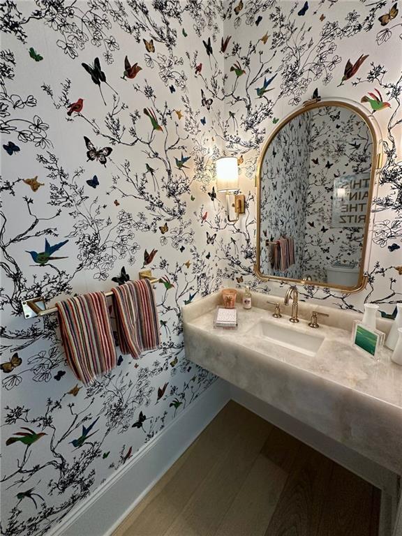 bathroom with a sink, baseboards, wood finished floors, and wallpapered walls