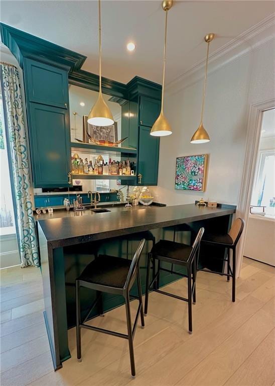 bar with pendant lighting, light wood-style flooring, ornamental molding, a sink, and wet bar