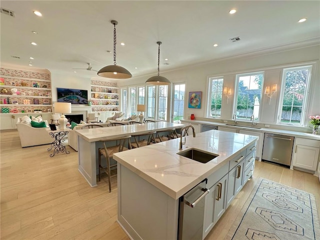 kitchen featuring an island with sink, a sink, dishwasher, crown molding, and light wood-type flooring