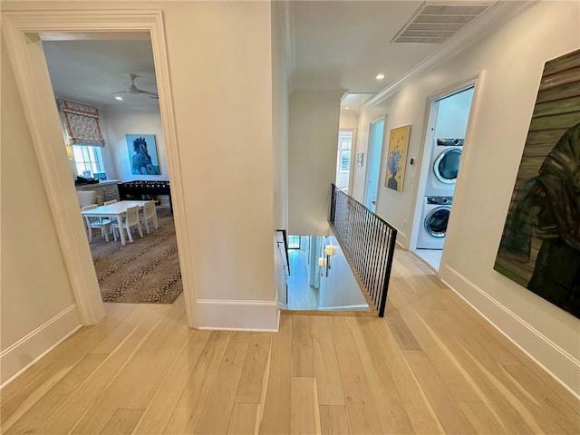 hallway with visible vents, crown molding, an upstairs landing, stacked washing maching and dryer, and wood finished floors